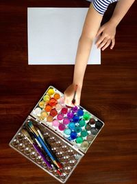 A child reaches with her paintbrush to the tray of watercolors