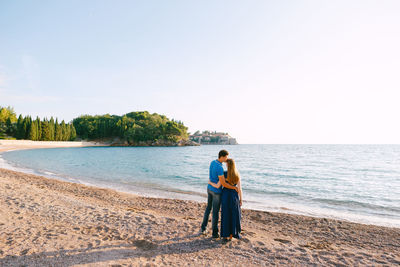 Rear view of couple on beach against sky