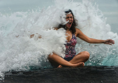 Waves splashing on woman sitting on rock at beach