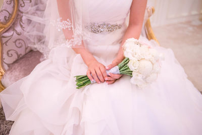 Midsection of bride with bouquet sitting on chair