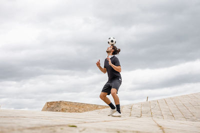 Man training with soccer ball against cloudy sky