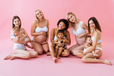 Portrait of happy friends sitting against white background