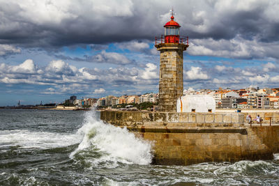 Lighthouse by sea against buildings in city