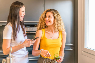 Smiling female friends talking while standing at home