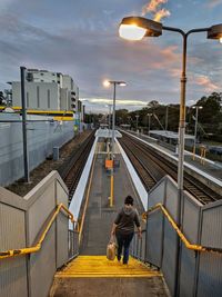 Rear view of woman moving down on staircase at railroad station platform against sky