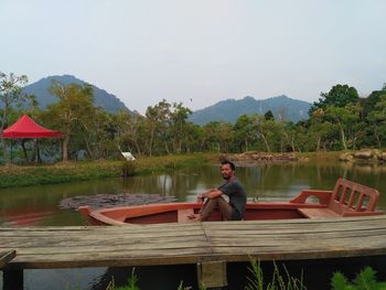 Man sitting by lake against sky