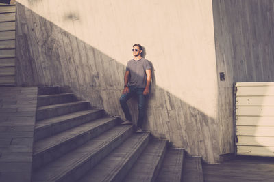 Full length portrait of young man standing on staircase against wall