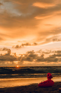 Rubber duck on beach against sky during sunset