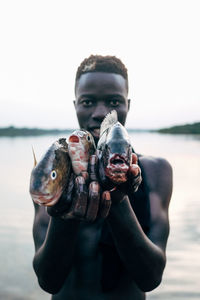 Close-up of young woman holding fish in sea against sky