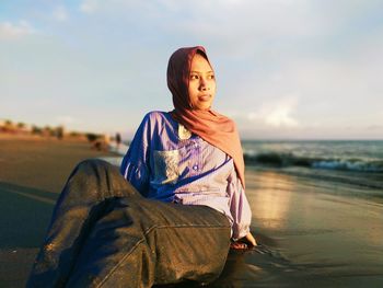 Portrait of young woman sitting by sea against sky