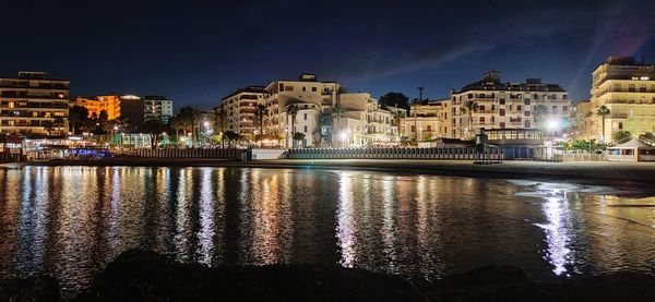 Illuminated buildings by river against sky at night