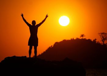 Silhouette man with arms raised standing against clear orange sky