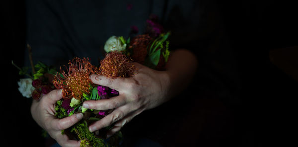 Midsection of person holding various flowers at night