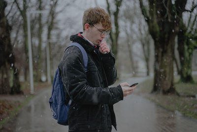 It's snowing, a guy in the park smokes an electronic cigarette and looks at a mobile phone
