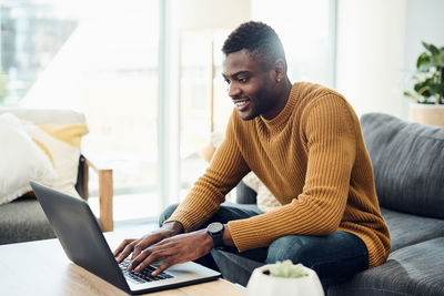 Young man using laptop while sitting on sofa at home