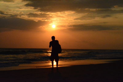 Rear view of silhouette man standing on beach during sunset