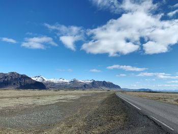 Road leading towards mountains against blue sky