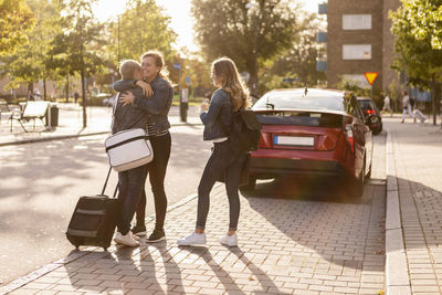 Full length of smiling mother embracing son while daughter standing at roadside