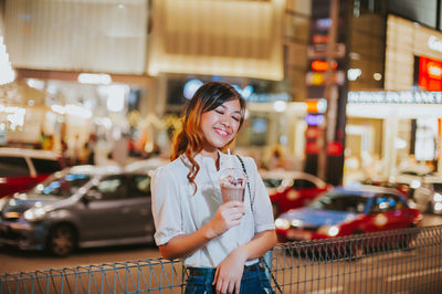 Full length portrait of woman standing against illuminated building