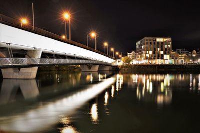 Illuminated bridge over river in city at night