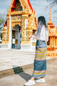 Rear view of woman standing outside temple against building