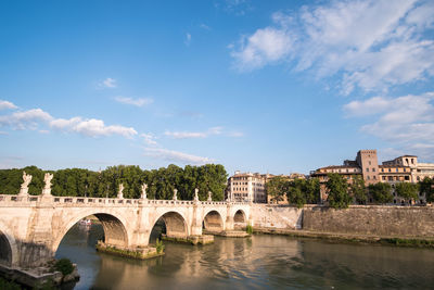 Arch bridge over river by buildings against sky