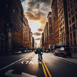 People riding bicycle on city street against sky