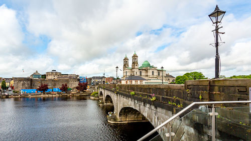 Bridge over river by buildings against sky in city