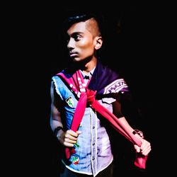 Portrait of young man standing against black background