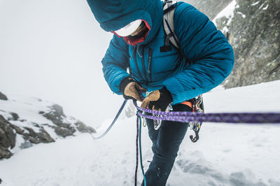 An alpine climber in a puffy jacket puts his belay device on ropes