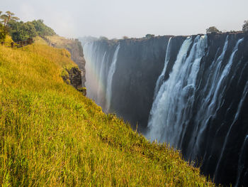 Scenic view of victoria falls with lush green and yellow grass against sky