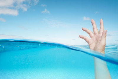 Cropped image of person drowning in sea against sky