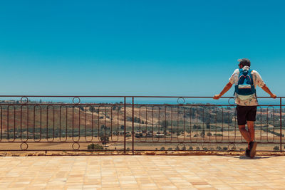 Man standing by railing against clear blue sky