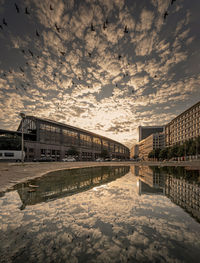 Bridge over canal by buildings against sky during sunset