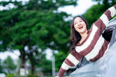 Portrait of smiling young woman standing against trees