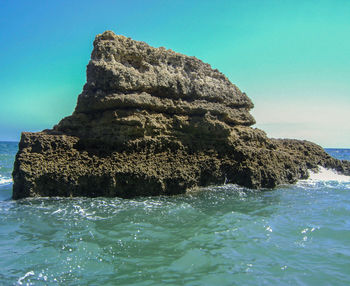 Rock formation in sea against clear blue sky