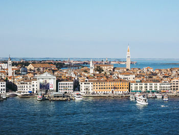 Aerial view of buildings by sea against clear sky during sunny day