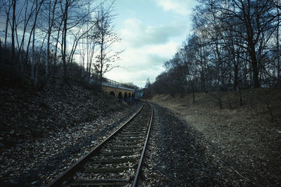 Railway tracks amidst bare trees against sky