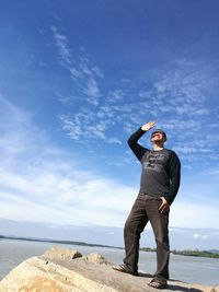 Full length of man standing on rock by lake against sky