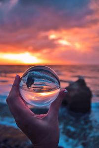 Midsection of person holding sea against sky during sunset