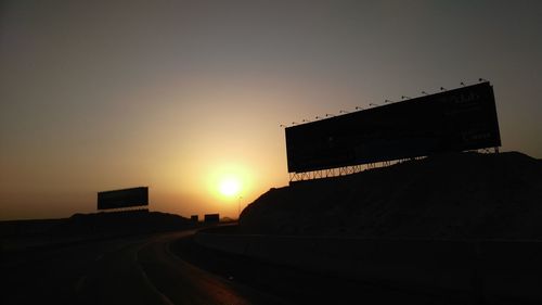 Road by silhouette city against sky during sunset