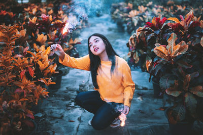 Full length of woman looking at burning firework amidst plants