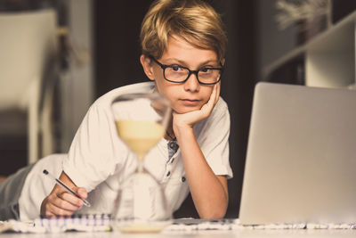 Cute boy looking at hourglass while sitting at table