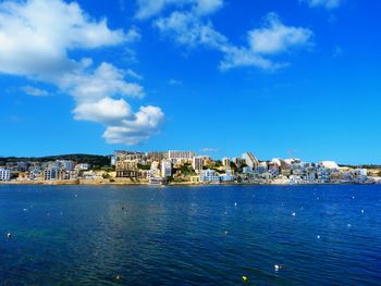 Buildings by sea against blue sky