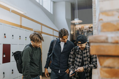 Happy male students sharing smart phone while standing in corridor