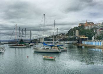 Boats in harbor against cloudy sky