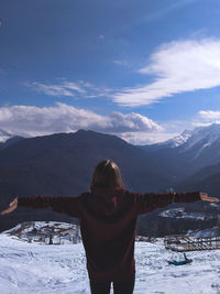 Rear view of woman standing on snowcapped mountain against sky