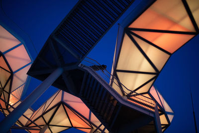 Low angle view of woman standing on footbridge against illuminated structure at dusk