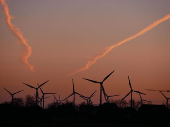 Silhouette wind turbines on land against sky during sunset