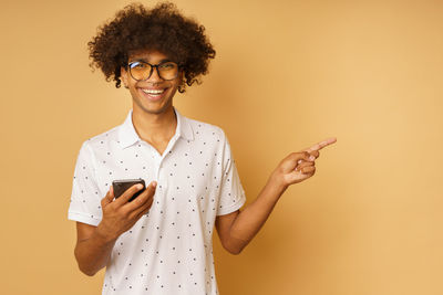 Smiling young man using mobile phone against orange background